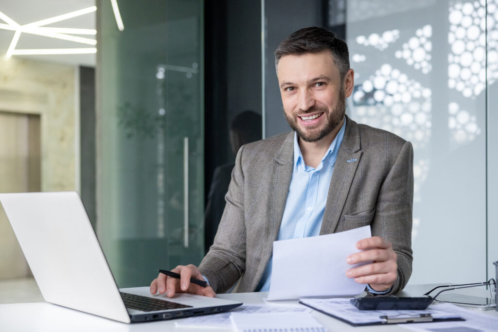 smiling businessman his desk working laptop checking documents contemporary office